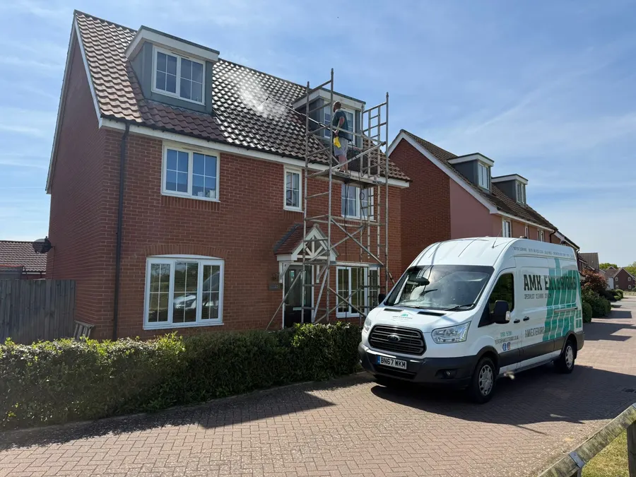 Technician cleaning a two-storey house roof from scaffolding with the AMK Exteriors van parked below